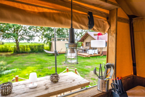 Vista desde la tienda safari Cozy Lodge con interior elegante, escena exterior y utensilios de camping.