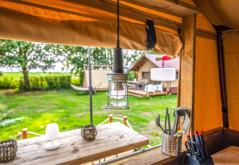 Gezicht vanuit de Cozy Lodge safaritent met stijlvol interieur, buitenscène en kampeerbenodigdheden.