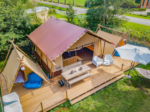 Aerial view of Cozy Lodge safari tent with wooden deck, outdoor seating, white chairs, and umbrella.