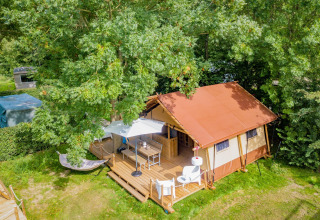 Vista aérea de la tienda safari Cozy Lodge con terraza de madera, sombrilla, sillas y hamaca en la naturaleza.