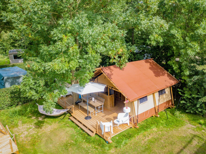 Vue aérienne d'une tente safari Cozy Lodge avec terrasse, parasol, chaises d'extérieur et hamac dans la verdure.