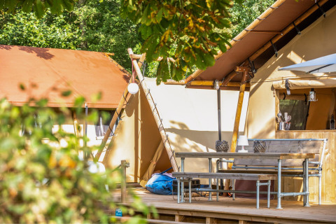 Terraza exterior frente a una tienda safari con banco, mesa y cocina en Cozy Lodge con baño privado.