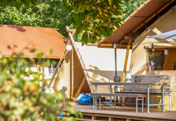 Outdoor terrace in front of a safari tent with bench, table and kitchen at Cozy Lodge with private bathroom.
