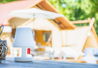 Lámpara de mesa con etiqueta roja sobre mesa de madera delante de tienda safari Cozy Lodge + sanitary.