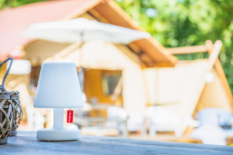 Table lamp with red tag sits on wooden table in front of a safari tent named Cozy Lodge + sanitary.