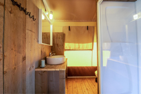 Baño de la tienda safari Cozy Lodge con paredes de madera, lavabo, espejo y luz ambiental suave.