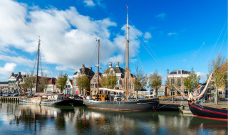 Sailing boats moored in a scenic harbor with historic buildings and blue sky, perfect holiday park view.
