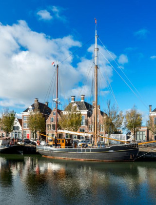 Barcos de vela atracados en un puerto pintoresco con casas históricas y cielo azul, ambiente vacacional.