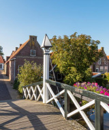 Puente de madera en un parque vacacional pintoresco con glamping, flores, canal y casas clásicas.