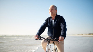 Hombre mayor monta en bicicleta en la playa de un parque vacacional con glamping, cielo soleado y tranquilo.