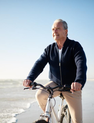 Hombre mayor monta en bicicleta en la playa de un parque vacacional con glamping, cielo soleado y tranquilo.