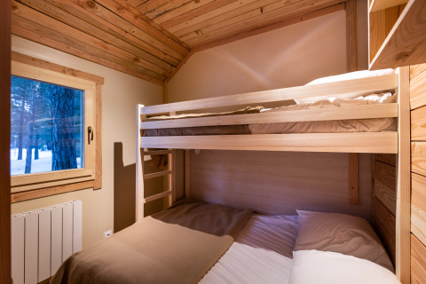 Acogedor dormitorio en el Chalet Montana con literas, paredes de madera y ventana con vistas al bosque nevado.