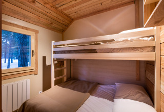 Hyggeligt soveværelse i Chalet Montana med køjeseng, trævægge og vindue med udsigt til sneklædt skov.