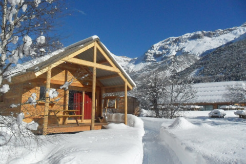 Cabaña de madera en Les Chalets Huttopia de Vallouise, Francia, rodeada de nieve y montañas nevadas.