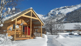 Cabaña de madera en Les Chalets Huttopia de Vallouise, Francia, rodeada de nieve y montañas nevadas.