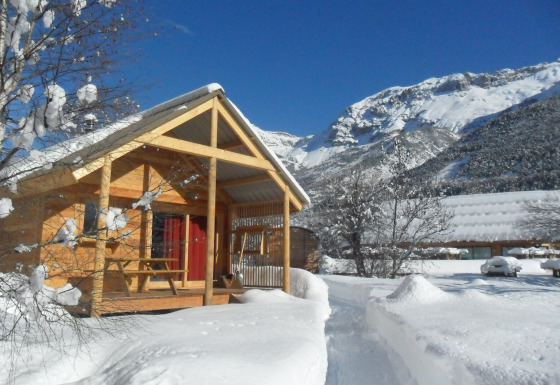 Cabaña de madera en Les Chalets Huttopia de Vallouise, Francia, rodeada de nieve y montañas nevadas.