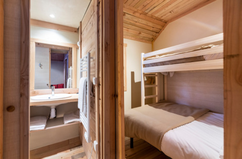 Interieur van een glampingverblijf met houten stapelbedden en badkamer in een warme, rustieke sfeer.