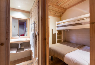 Habitación de glamping con literas de madera y baño, ambiente cálido y acogedor de estilo rústico.
