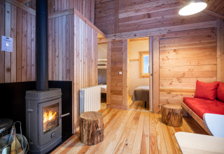 Interno di una accogliente cabina glamping con stufa a legna, pareti in legno e vista su camera e salotto.