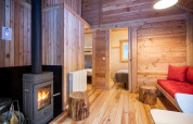 Gemütliche Glamping-Hütte mit Holzofen, Holzwänden und Blick auf Wohn- und Schlafzimmer im Inneren.