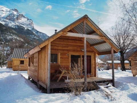 Houten chalet bij Les Chalets Huttopia de Vallouise, Frankrijk, omgeven door sneeuw en bergen.
