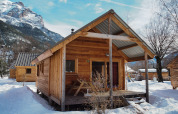 Cabaña de madera en Les Chalets Huttopia de Vallouise, Francia, rodeada de nieve y montañas.