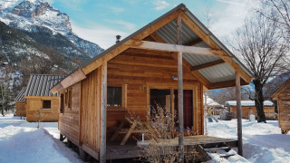 Cabaña de madera en Les Chalets Huttopia de Vallouise, Francia, rodeada de nieve y montañas.
