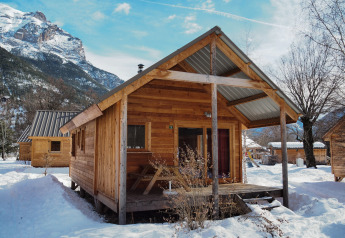 Cabaña de madera en Les Chalets Huttopia de Vallouise, Francia, rodeada de nieve y montañas.