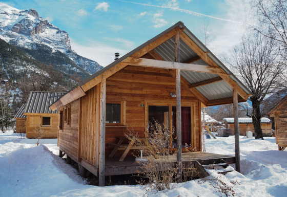 Chalet in legno a Les Chalets Huttopia de Vallouise, Francia, circondato da neve e montagne.