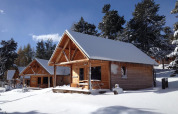 Besneeuwde houten chalets bij Les Chalets Huttopia de Font-Romeu in Frankrijk, tussen winterse bomen.