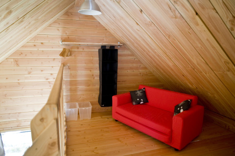 Hippe zolderruimte met houten panelen, rode sofa en opbergruimte in het chalet in Font-Romeu, Frankrijk.