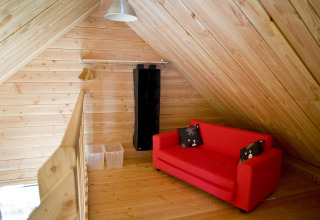 Et hyggeligt loftsrum med træpaneler, rød sofa, puder og opbevaring i træchalet i Font-Romeu, Frankrig.