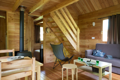 Intérieur du chalet en bois aux Chalets Huttopia de Font-Romeu en France, salon et cuisine visibles.