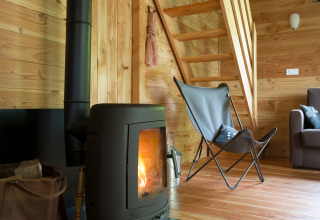 Intérieur de chalet en bois avec poêle à bois, fauteuil moderne et escalier, Les Chalets Huttopia Font-Romeu.