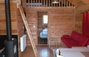 Innenraum des Chalet Montana Vista Glamping mit Holzwänden, Kamin, Schlafboden und Essbereich.