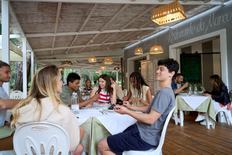 Jóvenes disfrutan de una comida juntos en una terraza cubierta en Campo dei Fiori, Glamping4all, Toscana, Italia.