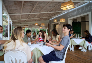 Young adults enjoy a meal together on a covered terrace at Campo dei Fiori, Glamping4all, Tuscany, Italy.