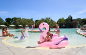 Bambini che giocano su fenicotteri gonfiabili nella piscina di Campo dei Fiori in Toscana, Italia.