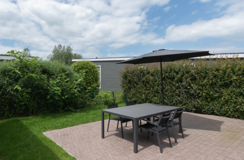 Udendørs terrasse med sort bord, fire stole og en parasol ved Access Lodge, Kompas Camping, Westende, Belgien.