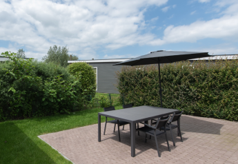 Terraza exterior con mesa negra, cuatro sillas y sombrilla en Access Lodge, Kompas Camping, Westende, Bélgica.