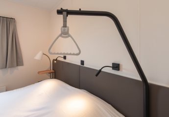 Dormitorio en Access Lodge en Kompas Camping Westende, Bélgica, con una grúa de asistencia sobre la cama.