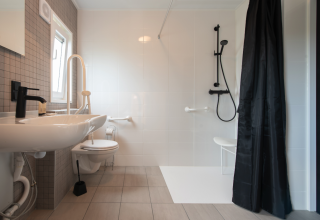 Toegankelijke badkamer met handgrepen, douchestoel en ruime indeling in Access Lodge, Kompas Camping.