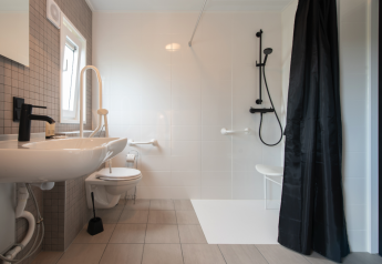 Baño adaptado con barras de apoyo, asiento de ducha y acceso amplio en Access Lodge, Kompas Camping, Bélgica.