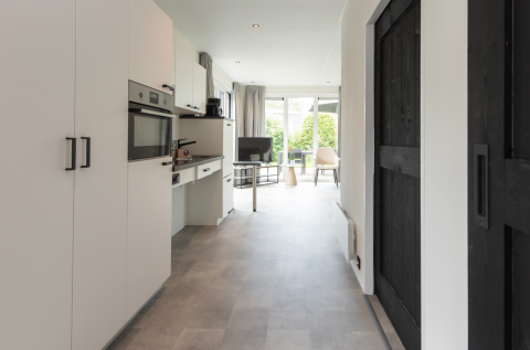 Moderne lodgekøkken og stue med store vinduer og udsigt til haven i Access Lodge, Kompas Camping Westende.