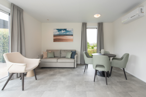 Moderne stue i Access Lodge med gråt møblement, spisebord, sofa og stort vindue med udsigt.