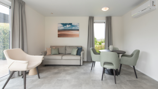 Modernes Wohnzimmer in der Access Lodge mit grauen Möbeln, Esstisch, Sofa und großem Fenster.