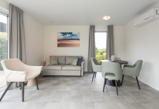 Moderne leefruimte in Access Lodge met grijze meubels, eettafel, zetel en groot raam.