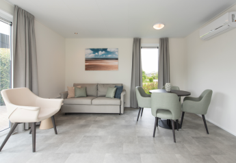 Salon moderne à Access Lodge avec mobilier gris, table à manger, canapé et grande fenêtre.