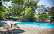 Udendørs swimmingpool omgivet af liggestole og parasoller i et grønt ferieparklandskab ved Huttopia le Moulin.