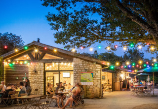 Buitenterras met feestverlichting en mensen aan het eten bij Huttopia le Moulin, Auvergne-Rhône-Alpes, Frankrijk.